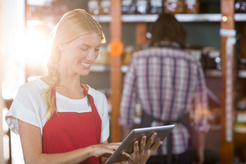Lächelndes weibliches Personal nutzt digitales Tablet im Supermarkt